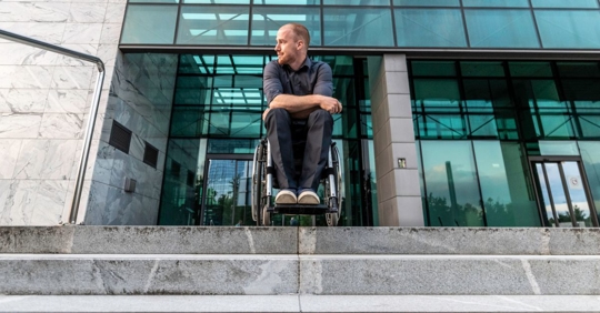 Businessman in wheelchair outside of his office building and sad